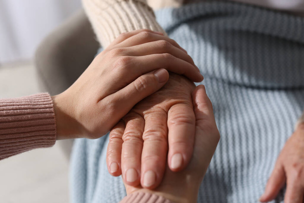 Young and elderly women holding hands together indoors, closeup - Foto, imagen
