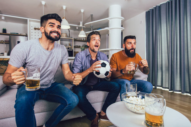 Bardzo podekscytowani przyjaciele bawią się oglądając mecz piłki nożnej w domu, w domu. Przyjaźń, leasing, sport, odpoczynek, koncepcja imprezy domowej - Zdjęcie, obraz