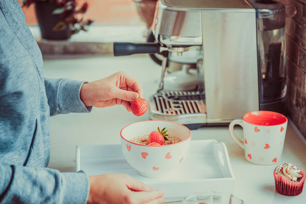 Woman adding strawberry fruits to oatmeal porridge bowl. Preparing surprise breakfast for lover on Valentines day. Simple festive healthy food idea. Copy space. Selective focus. - Fotografie, Obrázek