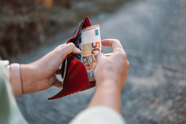 Unrecognizable female takes out 50 euro banknote from a red leather wallet on the street. Payment, salary and banking concept. - Fotó, kép