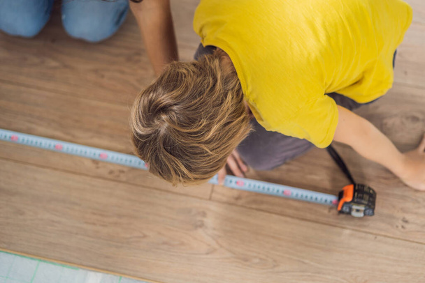 Father and son installing new wooden laminate flooring on a warm film floor. Infrared floor heating system under laminate floor - Φωτογραφία, εικόνα