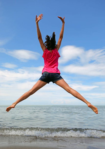 καυκάσια κορίτσια κάνουν ένα μεγάλο άλμα με ανοιχτά χέρια και πόδια δίπλα στη θάλασσα το καλοκαίρι - Φωτογραφία, εικόνα