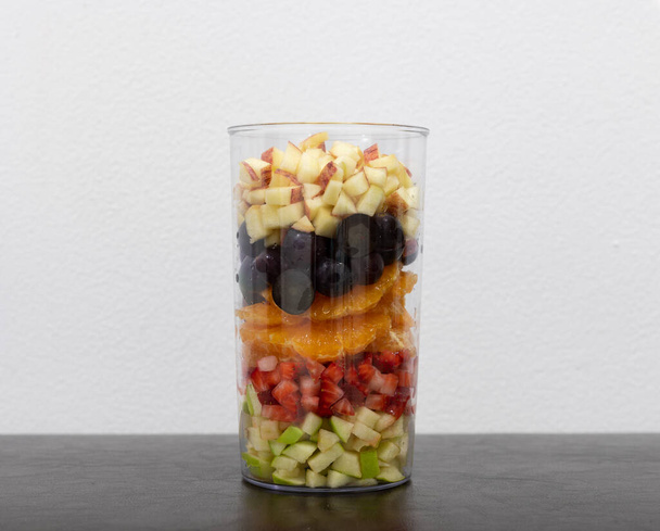 Широкое разнообразие срезанных фруктов помещается в стеклянную банку слоями. Концепция подготовки десерта. - Фото, изображение