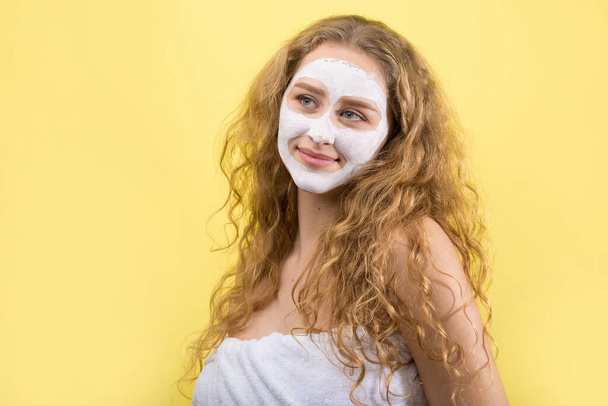 Chica con una máscara cosmética en su cara en una toalla blanca. - Foto, imagen