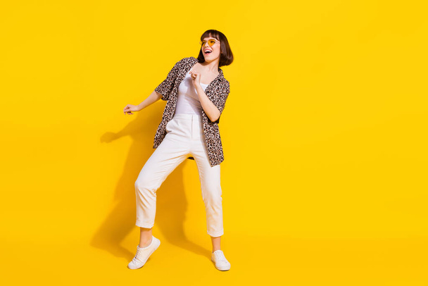 Full size photo of impressed lady dance look empty space wear eyewear shirt trousers sneakers isolated on yellow color background - Fotoğraf, Görsel