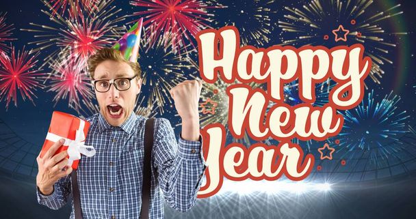 Digital composite image of young man holding gift cheering by happy new year text against firework. celebration, party and symbol. - Fotó, kép