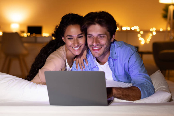 Lächelndes Paar mit Laptop schaut lustigen Film im Schlafzimmer - Foto, Bild