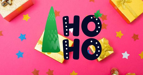 Digital composite image of hoho text and pine tree over presents amidst stars on pink table. christmas celebration and culture. - Foto, afbeelding