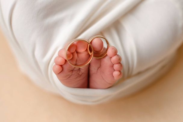 Маленькие ножки новорожденного ребенка с обручальными кольцами его родителей на пальцах. Семейные традиции - Фото, изображение
