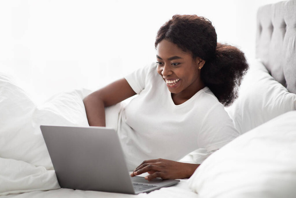 Vrolijke Afrikaanse Amerikaanse dame surfen op internet in bed - Foto, afbeelding