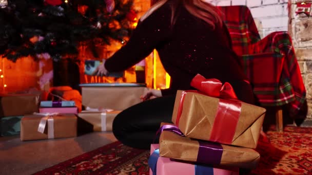 Mulher caucasiana sentada no chão ao lado da árvore de Natal decorada e escondendo caixas de presentes sob ele - Filmagem, Vídeo
