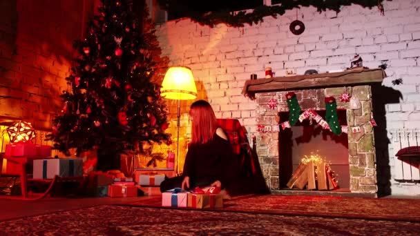 Mulher estabelece caixas embaladas de presentes sob uma árvore de Natal enquanto sentado no chão à noite - Filmagem, Vídeo
