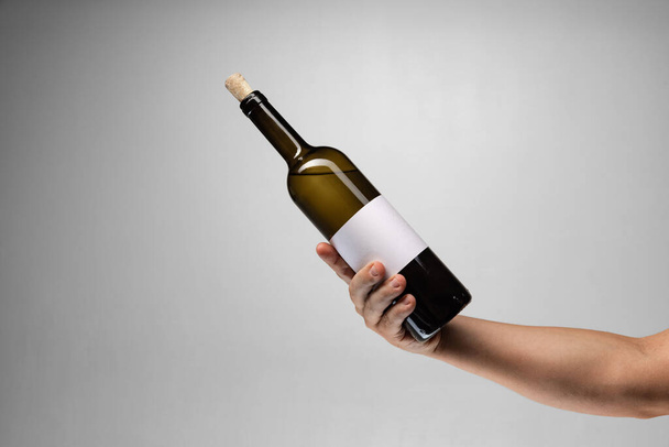 Image recadrée d'une main féminine tenant une bouteille de vin délicieux isolé sur fond gris - Photo, image
