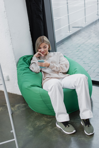 szczęśliwy menedżer siedzi na krześle worek fasoli i za pomocą smartfona  - Zdjęcie, obraz