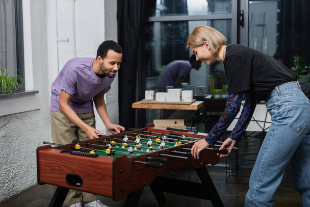 african american manager playing table football with happy blonde colleague - Photo, Image