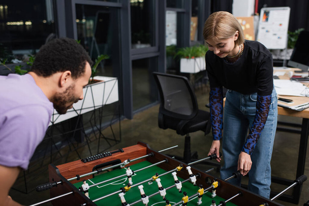 blurred african american manager playing table football with happy blonde colleague - Foto, afbeelding