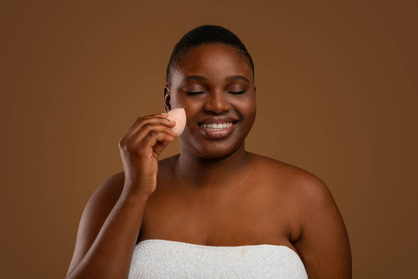 Black chubby woman with acne applying makeup with sponge - Fotoğraf, Görsel