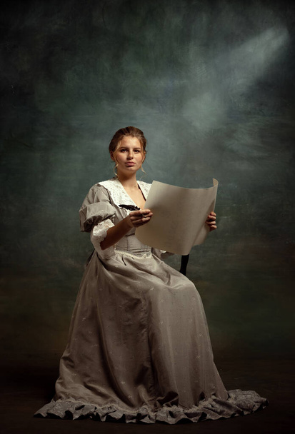 Vintage portrait of young beautiful girl in gray dress of medieval style isolated on dark background. Comparison of eras concept, flemish style. - Φωτογραφία, εικόνα