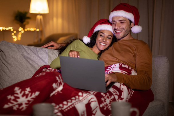 Casal assistindo filmes de Natal no laptop vestindo chapéus de Santa interior - Foto, Imagem