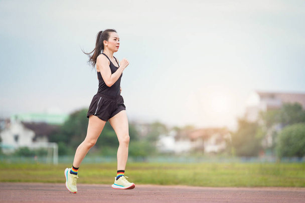 Dojrzała Azjatka biegnie biegając po stadionie w słoneczny poranek, aby utrzymać kondycję i zdrowy tryb życia. Aktywny zdrowy biegacz jogging na świeżym powietrzu - Zdjęcie, obraz