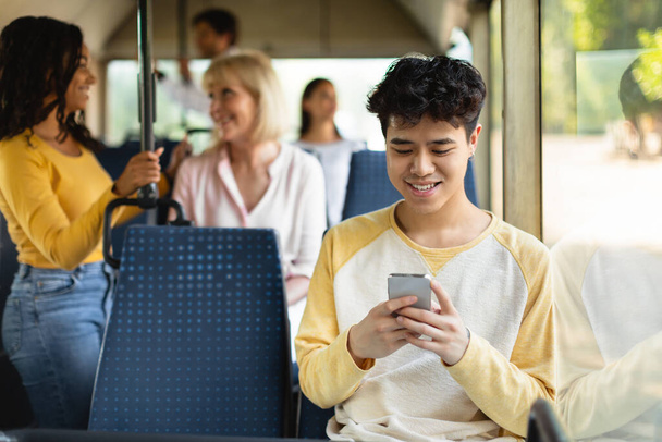 幸せなアジアの男使用して携帯電話でバス - 写真・画像