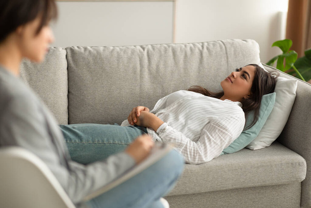 Paciente mujer árabe joven acostada en el sofá en la oficina de psicólogos, teniendo una sesión con el consejero - Foto, Imagen