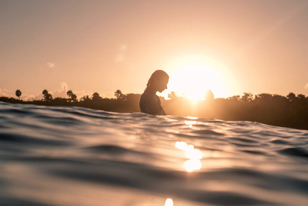Retrato de una surfista rubia sobre tabla de surf blanca en el océano azul fotografiada desde el agua al amanecer dorado en la playa Encuentro en República Dominicana - Foto, imagen