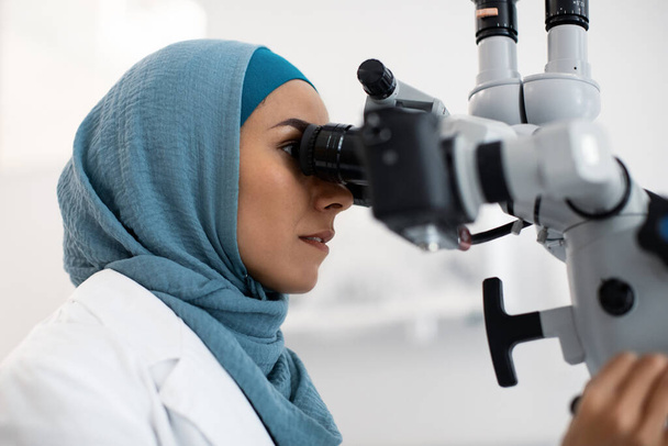 Trabajadora médica musulmana en Hijab usando microscopio dental en clínica moderna - Foto, imagen