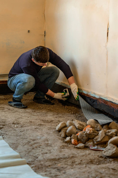 Der Arbeiter befestigt ein Bitumenband mit einem Hefter, um Holz und Boden vor Wasser, Abdichtung und Schutz zu schützen. - Foto, Bild
