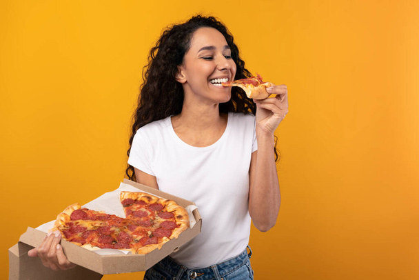 Happy Latin Woman Holding Box Biting Pizza At Studio - Foto, immagini
