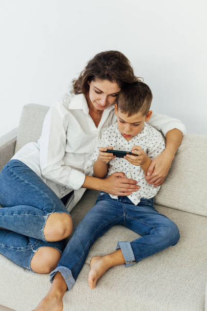 красивая мать и сын на диване, смотрящие смартфон интернет - Фото, изображение