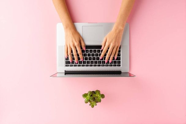 Female hands using laptop on pink background. Office desktop. Top view - Foto, imagen
