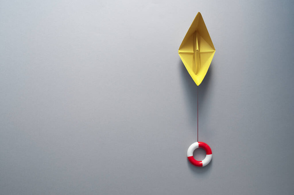 Buoy attached to paper boat symbolising business recovery, insurance, and rescue - Valokuva, kuva