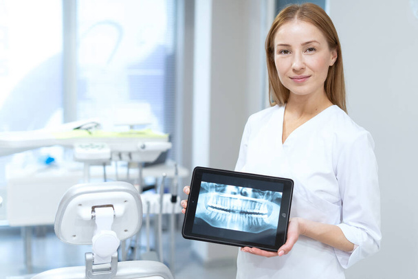 Portrait of dentist holding tablet with tooth panoramic x-ray image. Orthopantomogram scan. Modern technology in stomatology. Oral medicine concept - Foto, afbeelding