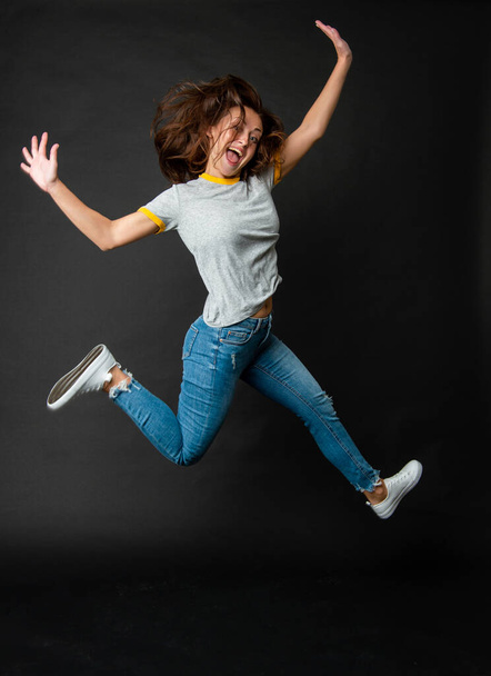 Happy cool ecstatic energetic girl jumping up midair dark background, jump - Fotó, kép