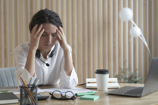 Уставшая испанская бизнесвумен с закрытыми глазами сидит на рабочем месте в офисе, страдая от головной боли - Фото, изображение