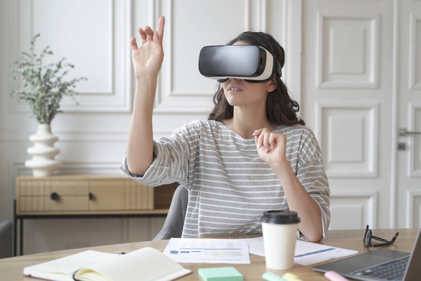 Mujer joven enfocada que usa auriculares de realidad virtual viendo contenido de 360 grados en el trabajo - Foto, imagen