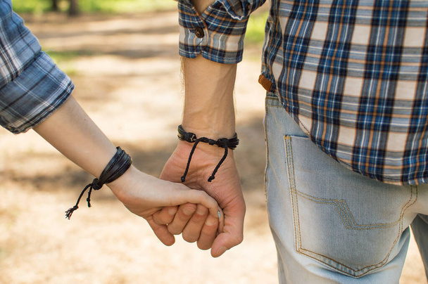 Hands of lovers in the forest. a couple of lovers are holding hands. on the hands of identical leather bracelets. - Photo, Image