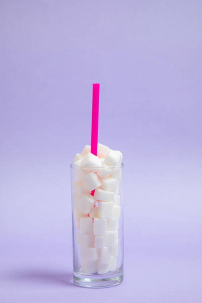 glass full of sugar cubes with a straw inside on a purple background. Cool photo, refreshing joyful idea. Sugar drink. - Foto, Bild