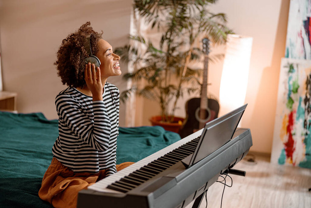 Веселая женщина в наушниках играет на синтезаторе дома - Фото, изображение