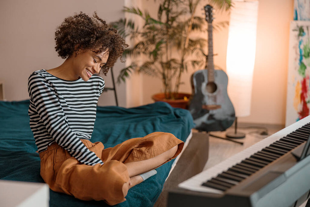 Mujer alegre sentada cerca del sintetizador en casa - Foto, imagen