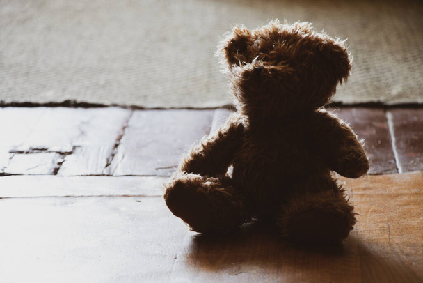 oso de peluche marrón se sienta en un viejo piso de madera en una habitación oscura, juguetes para niños en el suelo, miedo - Foto, Imagen