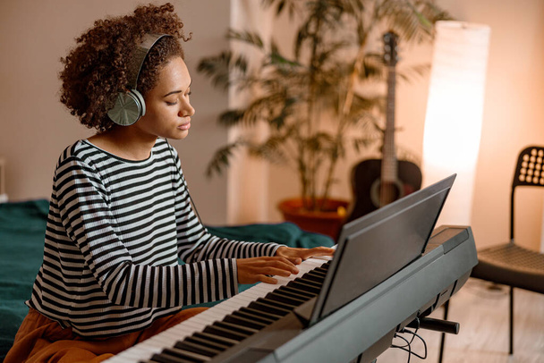 Молодая женщина в наушниках играет на синтезаторе дома - Фото, изображение