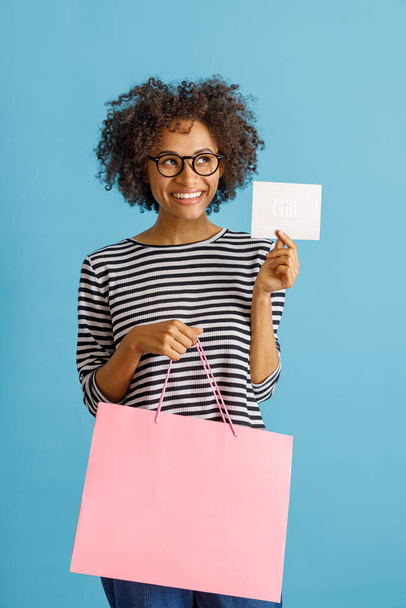 Joyful woman holding shopping bag and gift card - Фото, изображение