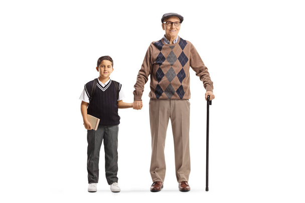 Full length portrait of a grandfather and grandson in a school uniform standing and holding hands isolated on white background - Foto, Bild