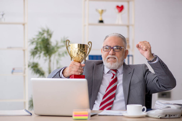 Alter männlicher Mitarbeiter wird mit goldenem Pokal ausgezeichnet - Foto, Bild