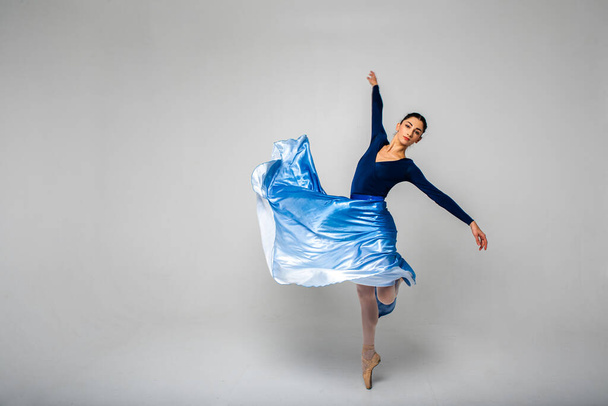 Gyönyörű balerina tánc mutatja a különböző gyakorlatok nézett egyenesen a kamerába egy hosszú kék ruhát, világos háttérrel. Szelektív fókusz, mozgás - Fotó, kép