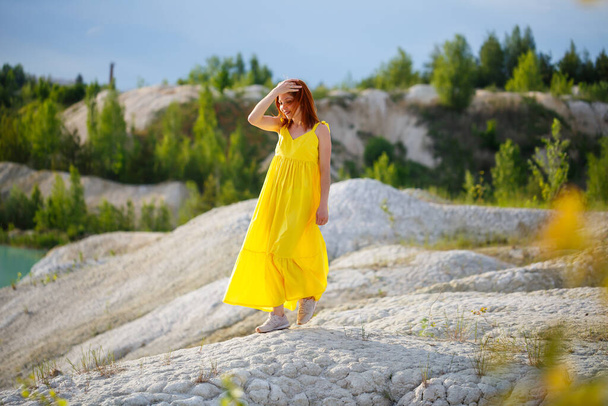 Jovem mulher em um vestido amarelo perto do lago com água azul e árvores verdes. - Foto, Imagem