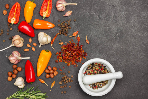 Fresh peppers, nuts, garlic and rosemary on table. Allspice in mortar. Copy space. Flat lay. Black background - Photo, image