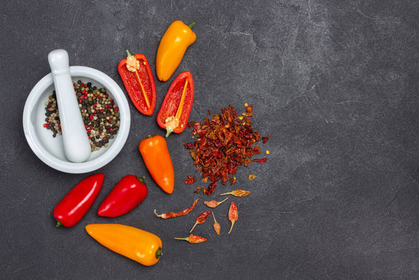 Fresh red and yellow peppers, nuts, dry pods and pepper petals on table. Allspice in mortar. Copy space. Flat lay. Black background - Foto, Bild